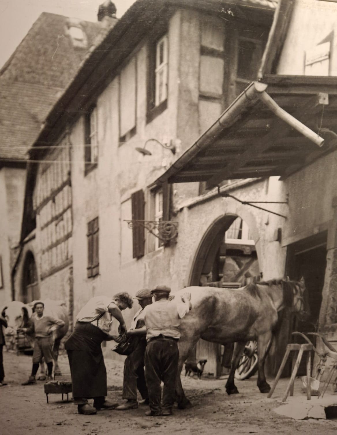 Photo d'archive de la maison à colombages et de la rue du village, avec un maréchal-ferrant ferrant un cheval